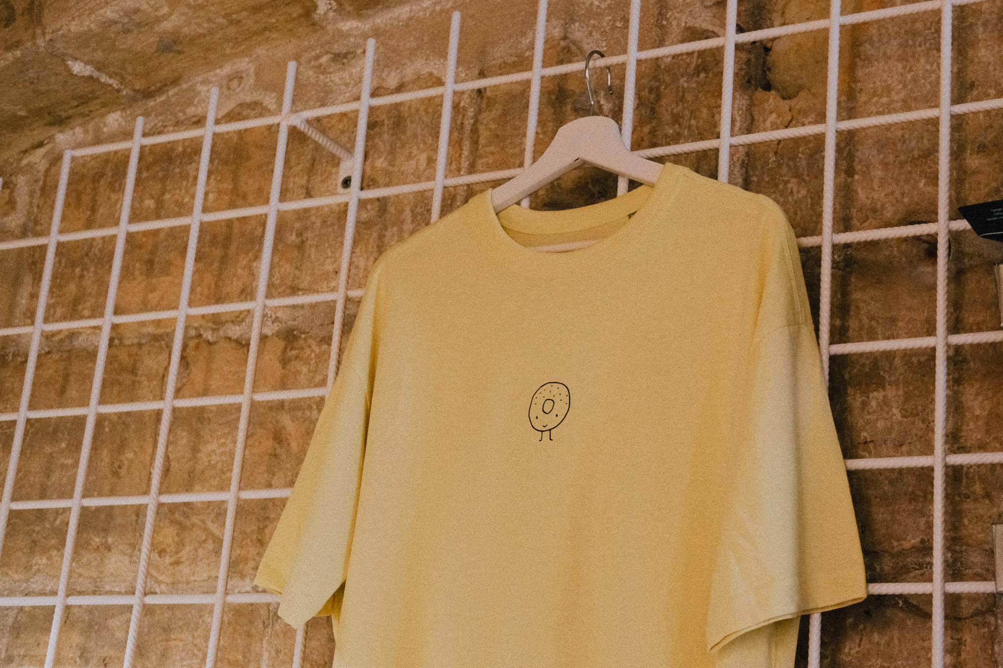 "100% cotton boxy t-shirt featuring a casual fit, displayed on a hanger against a stone background showcasing the bagel shop's logo."